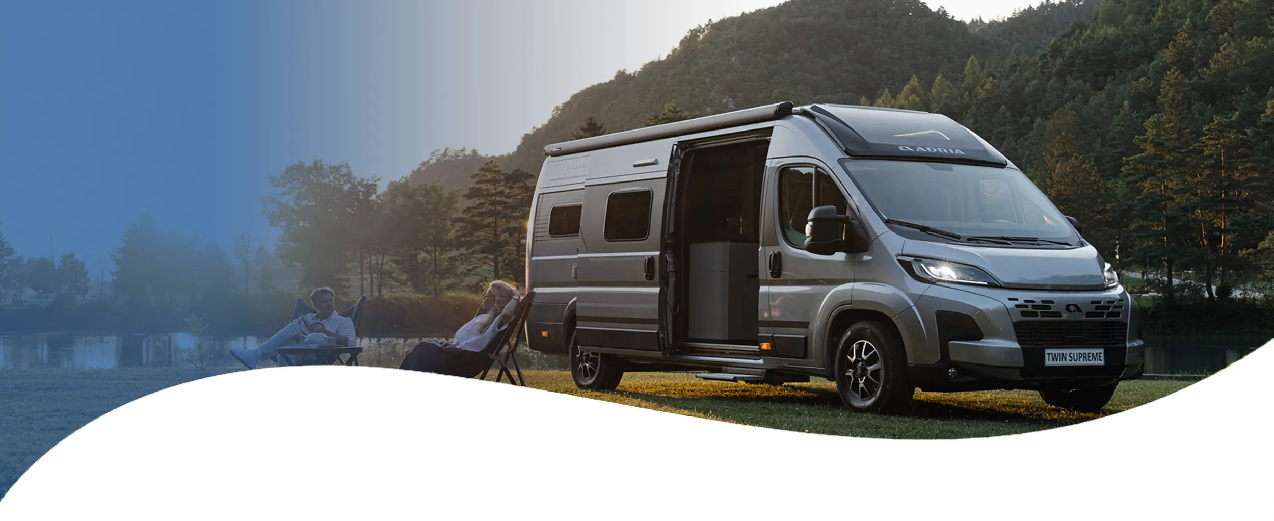 Adria Wohnwagen, davor sitzen zwei Camper