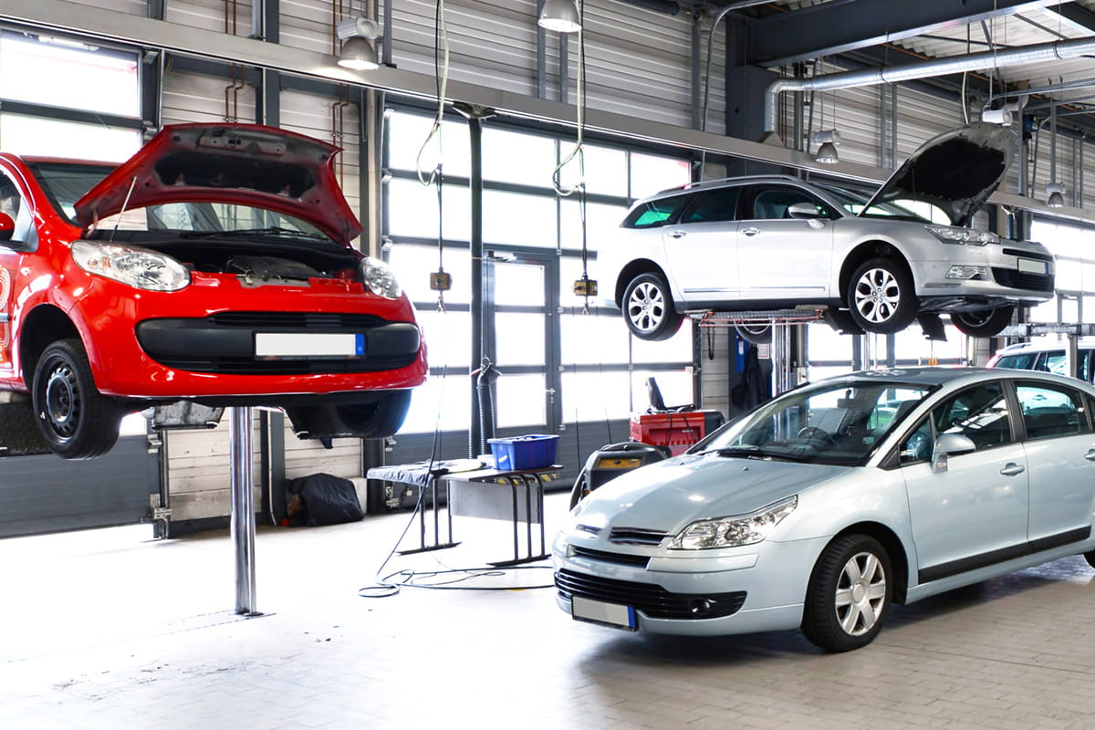 zu sehen sind zwei Autos auf einer Hebebühne, davor steht ein Auto in der Werkstatt