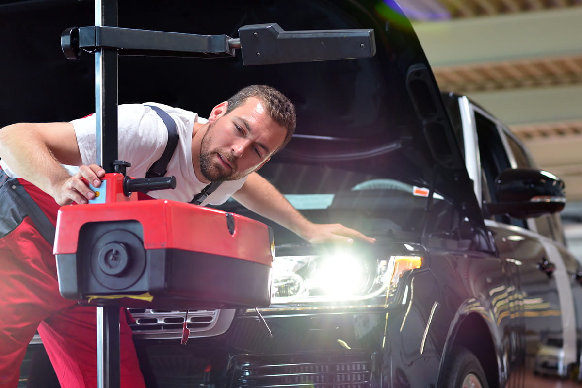 zu sehen ist ein KFZ Mitarbeiter, der einen Scheinwerfer prüft